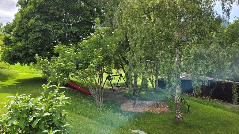 Flackl-Wirt - Schaukel, © Flackl - Wirt GmbH & Co KG Ein grüner Garten mit Bäumen, einer Schaukel und einer Rutsche.