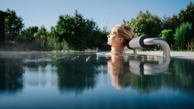 Therme Laa, Außenbereich, © Thermenresort Laa / Pflanzl Media Eine Frau entspannt sich in einem Außenpool, umgeben von grüner Natur und klarem Himmel.