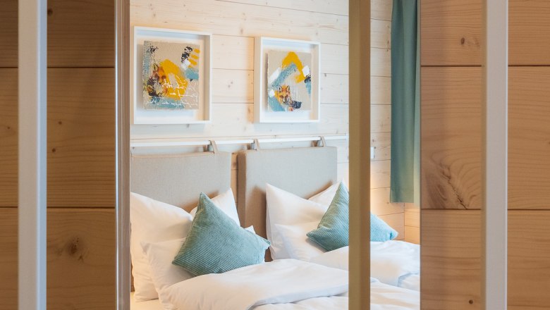 Doppelzimmer, © freilich / IsaBella Fritsche Ein gemütliches Doppelzimmer mit Holzverkleidung, zwei Betten, blauen Kissen und moderner Kunst an der Wand.
