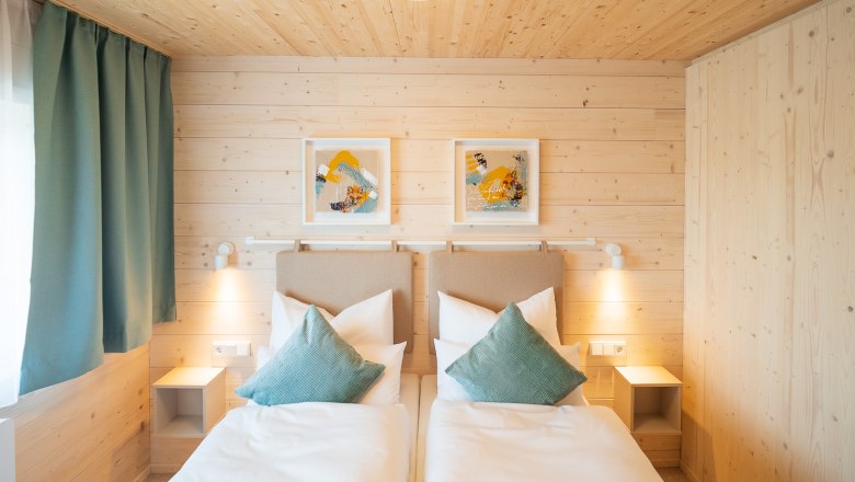 Gemütliches Doppelbett, © freilich / IsaBella Fritsche Gemütliches Schlafzimmer mit zwei Einzelbetten, Holzwänden und moderner Dekoration.