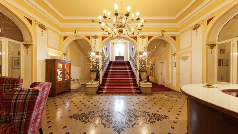 Marienhof Lobby, © Hotel Marienhof Elegante Lobby mit rotem Teppich, Treppe und Kronleuchter.