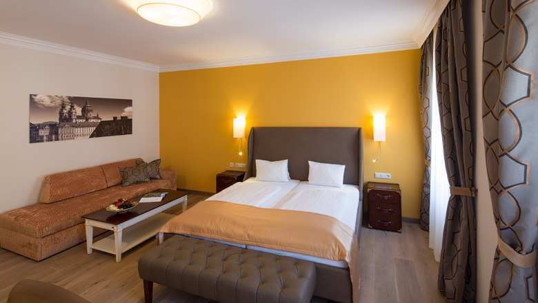 Zimmerbeispiel im Hotel-Restaurant Zur Post, © Lachlan Blair Hotelzimmer mit Doppelbett, gelber Wand, Sofa, Tisch und Vorhängen.