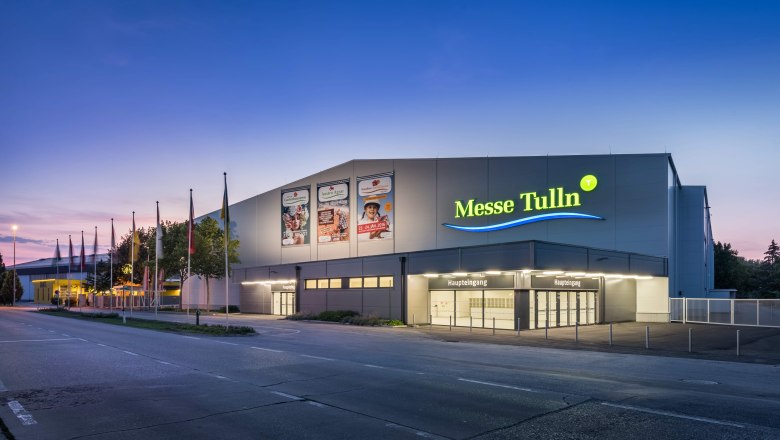Messe Tulln, © Jansenberger Außenansicht der Messe Tulln bei Dämmerung mit beleuchtetem Eingang und Fahnen.