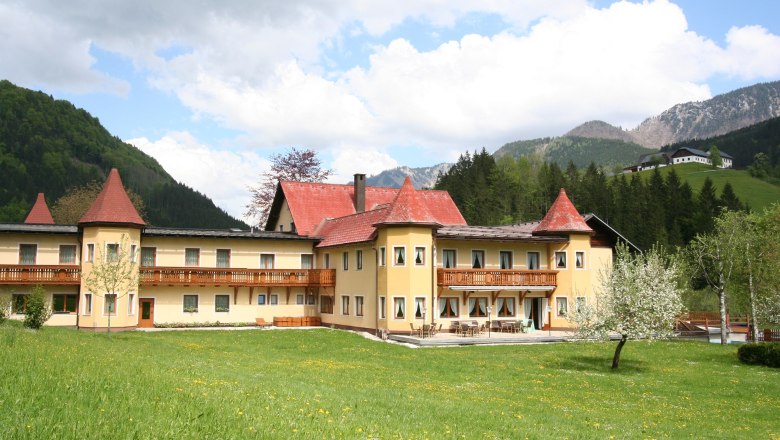 Hotel Waldesruh, © Hotel Waldesruh Ein großes Hotel mit roten Dächern in einer grünen, bergigen Landschaft.