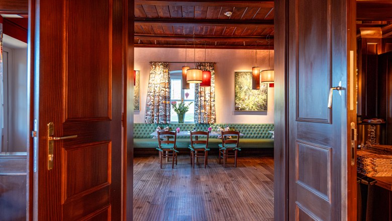 Hotel & Restaurant Knappenhof, © Niederösterreich Werbung / Maximilian Pawlikowsky Blick durch geöffnete Holztüren in einen gemütlichen Raum mit Holzboden, Tisch und Stühlen, dekoriert mit Lampen und Vorhängen.