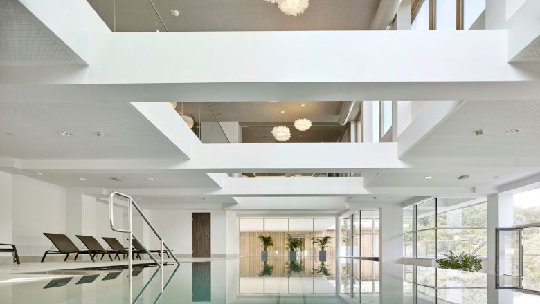 Steigenberger Krems, Innenpool, © Steigenberger Hotel and Spa, Gregor Titze Indoorpool mit Liegestühlen und großen Fenstern.