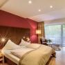 Zimmer, © Hotel Krainerhütte Modernes Hotelzimmer mit Doppelbett, roter Wand, großem Fenster und Sitzbereich.