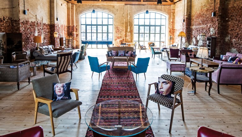 Schloss Grafenegg, Alte Scheune, © Nik Pichler Innenansicht einer stilvoll eingerichteten Scheune mit Holzboden, gemauerten Wänden und großen Fenstern. Verschiedene Sitzmöbel und bunte Kissen sind zu sehen.