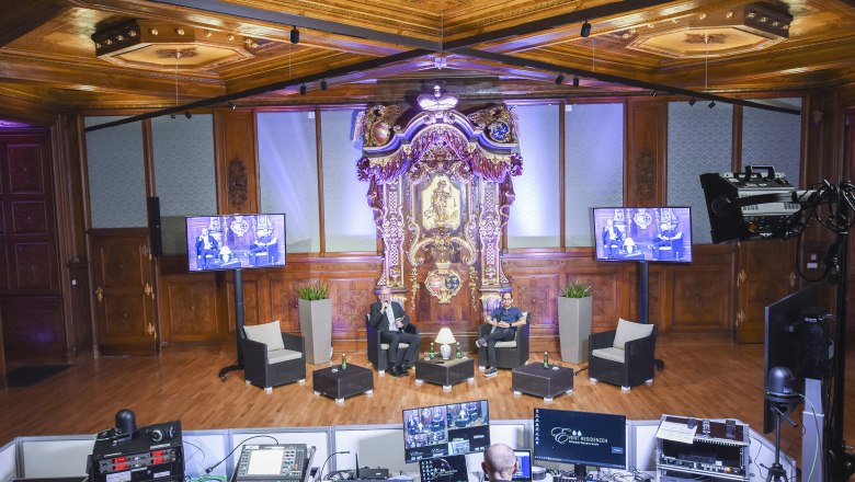 Palais Niederösterreich, Studio 13, © Event Residenzen Niederösterreich Ein opulenter Raum mit Holzvertäfelung und einem aufwendigen Altar. Zwei Personen sitzen auf einer Bühne, umgeben von Technik und Bildschirmen.