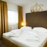 Doppelzimmer Bett, © Hotel Kaiser Franz Josef Ein Doppelzimmer mit einem großen Bett, goldenen Vorhängen und zwei Nachttischen mit Lampen.