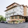 R&R Residenzen Hotel, © Robert Karner Ein modernes Hotelgebäude mit Holzverkleidung und Balkonen, umgeben von Bäumen und einem Parkplatz mit Autos.