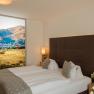Donauhof Doppelzimmer, © Marcella Wallner Modernes Hotelzimmer mit Doppelbett, dekorativen Kissen und großem Landschaftsbild an der Wand.
