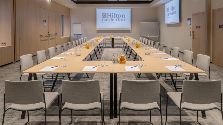 Hilton Garden Inn, Meeting Raum, © Hilton Garden Inn Wiener Neustadt Ein moderner Meetingraum im Hilton Garden Inn mit U-förmiger Tischanordnung, Stühlen, Wasserkrügen und Schreibmaterialien.