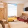 Zimmer im Hotel Donauhof, © Pichler Modernes Hotelzimmer mit Doppelbett, rotem Sofa, Flachbildfernseher und großem Fenster mit Landschaftsausblick.