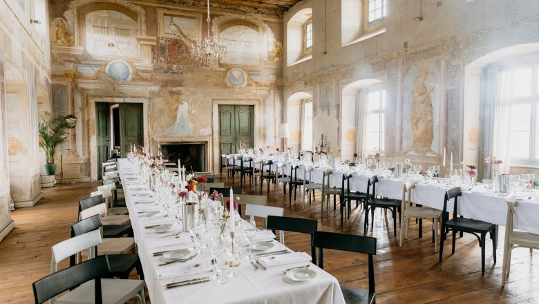 Schloss Haggenberg, © weddings by avocadi Eleganter Speisesaal in einem Schloss mit langen, gedeckten Tischen und Wandmalereien.