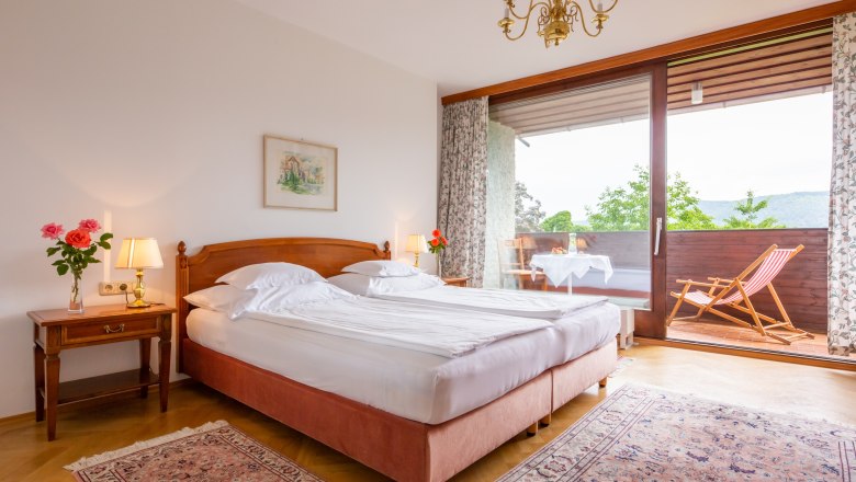 Zimmer im Hotel Richard Löwenherz, © Chris Saupper Ein gemütliches Schlafzimmer mit Doppelbett, Nachttischlampen und Balkon mit Liegestuhl und Tisch.