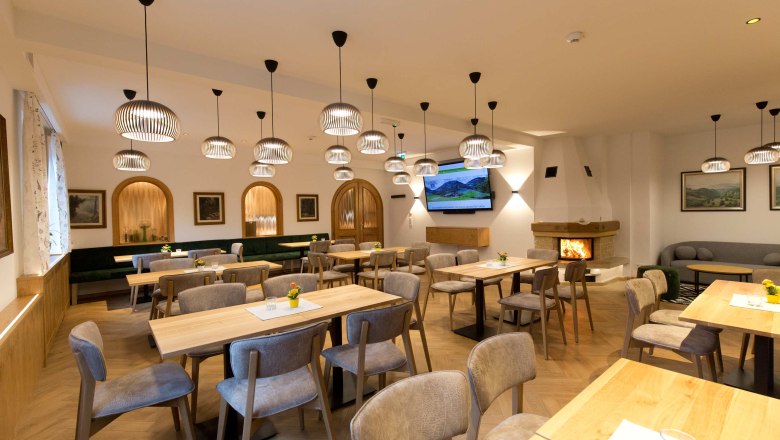 Flackl-Wirt - Kaminzimmer, © Flackl - Wirt GmbH & Co KG Ein gemütliches Kaminzimmer mit Holztischen, Stühlen und modernen Lampen. Ein Kamin brennt im Hintergrund.