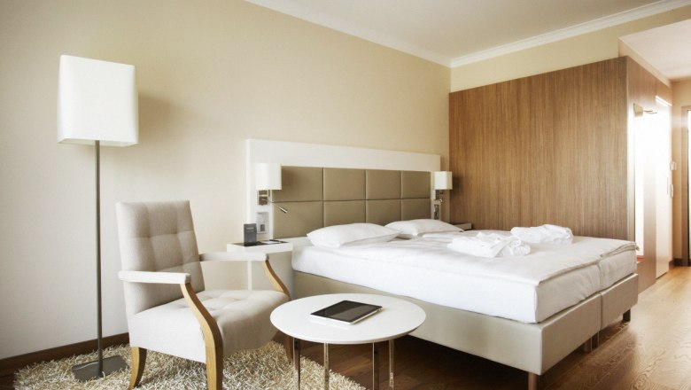 Steigenberger Hotel and Spa Krems, © Steigenberger Hotel and Spa Krems/Andreas Hofer Modernes Hotelzimmer mit Doppelbett, Sessel, Tisch und Stehlampe.