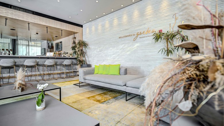 Hilton Garden Inn Wiener Neustadt, © Hilton Garden Inn Wiener Neustadt Moderne Hotel-Lobby mit Bar, grauen Sofas und grünen Kissen im Hilton Garden Inn Wiener Neustadt.