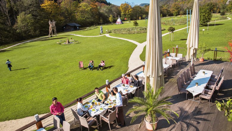 Seminar- und Eventhotel Krainerhütte, © Krisztian Juhasz Terrasse des Seminar- und Eventhotels Krainerhütte mit Gästen beim Essen, umgeben von grüner Wiese und Wald.