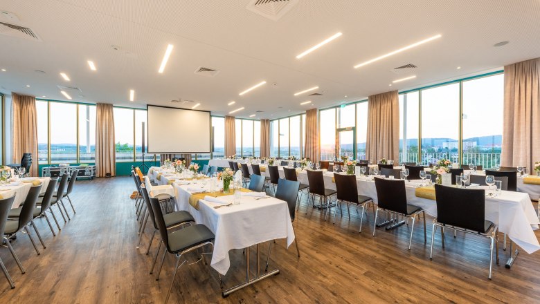 campus Horn, Saal Weitblick, © campus Horn Ein großer, heller Saal mit gedeckten Tischen und Stühlen, großen Fenstern und einem Projektor.