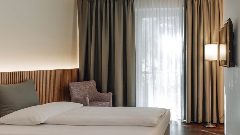 Comfort HEINhotel vienna airport, © HEINhotel vienna airport Modernes Hotelzimmer mit Bett, Sessel und Vorhängen.