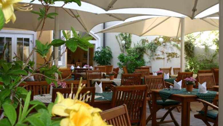 Gastgarten im Hotel-Restaurant Zur Post, © Hotel-Restaurant Zur Post Ein gemütlicher Gastgarten mit Holzmöbeln und Sonnenschirmen, umgeben von Pflanzen.