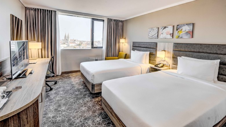 Hilton Garden Inn Wiener Neustadt, © Hilton Garden Inn Wiener Neustadt Hotelzimmer mit zwei Betten, Schreibtisch und Fenster mit Stadtblick.