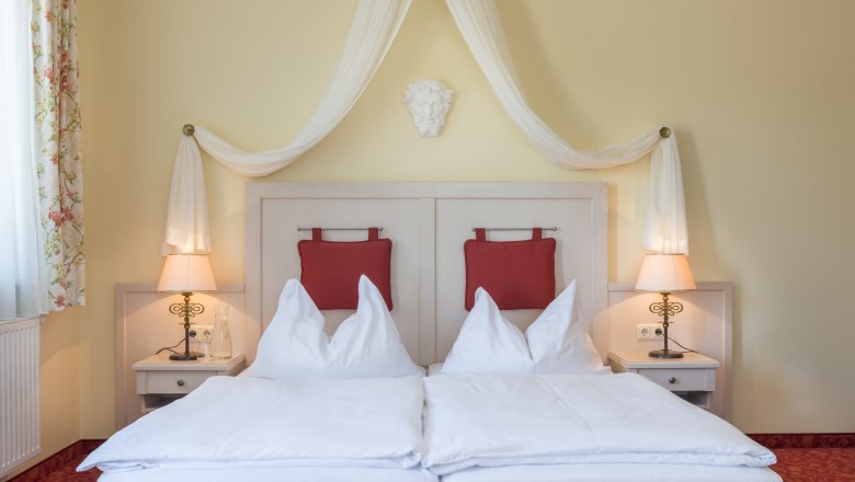 Zimmeransicht mit Himmelbett und roten Polstern