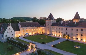 Luftaufnahme von Schloss Walpersdorf bei Dämmerung, beleuchtet mit Gästen bei einem Gartenfest im Innenhof.