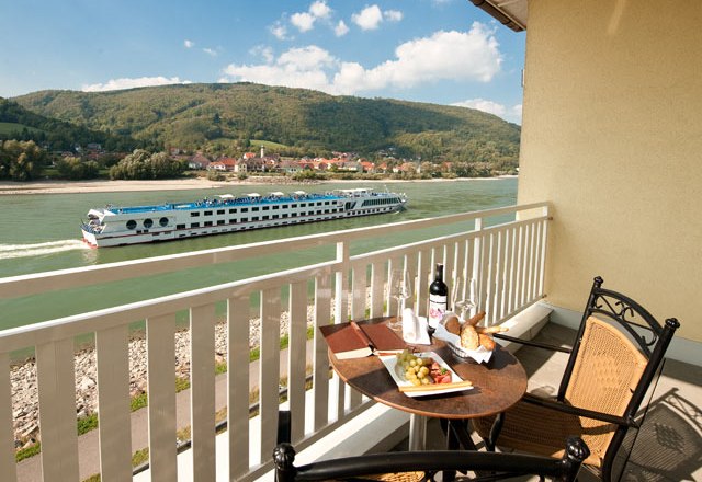 Balkon mit Tisch, Wein und Snacks, Blick auf Fluss und vorbeifahrendes Schiff.