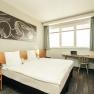 Modernes Doppelzimmer mit gro&szlig;em Bett, Kunstwerk an der Wand, Schreibtisch und Blumenarrangement.