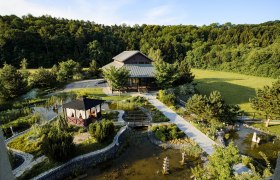 Asiatisch gestalteter Garten mit Pavillon und Teich, umgeben von Wald.