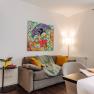 Wohnzimmer mit grauem Sofa, bunter Comic-Kunst an der Wand, gelben Vorh&auml;ngen und Fr&uuml;hst&uuml;ckstisch.