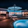 Nachtaufnahme eines modernen Spa-Bereichs mit beleuchteten Pools und einem gro&szlig;en Sonnenschirm.