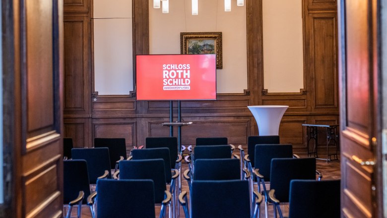 Ein Seminarraum im Schloss Rothschild mit Stuhlreihen, einem Bildschirm und einem Stehtisch.