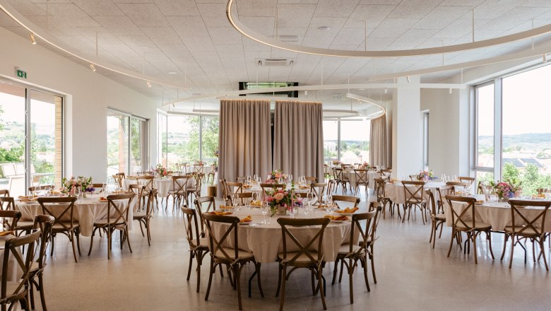 Eleganter Veranstaltungsraum mit runden Tischen, St&uuml;hlen und Blumendekoration.