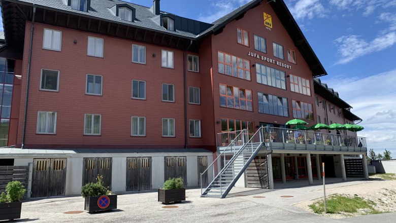 JUFA Sport Resort Hochkar mit roter Fassade und Terrasse mit gr&uuml;nen Sonnenschirmen.