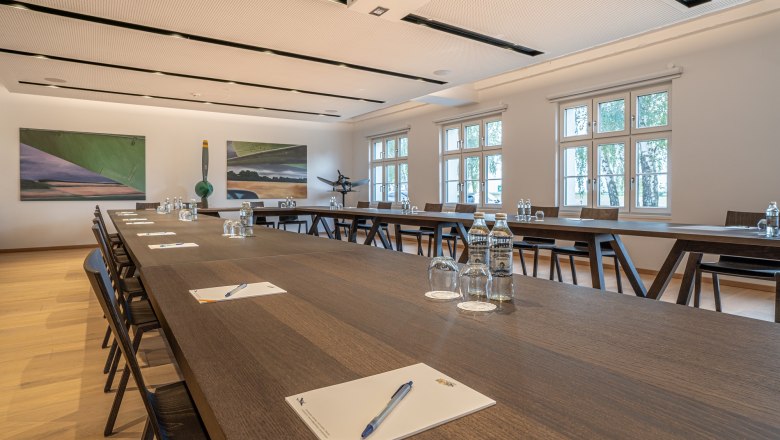 Seminarraum im Hotel Spitzerberg mit langen Holztischen, Stühlen, Wasserflaschen und Schreibmaterialien.