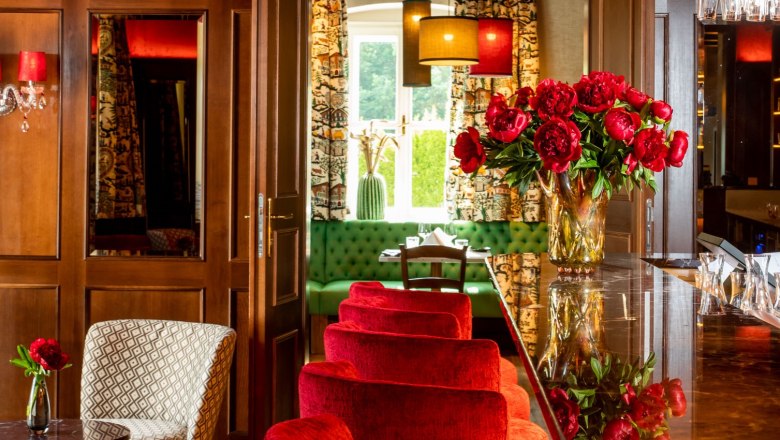 Elegantes Restaurant mit roten Samtst&uuml;hlen, Kronleuchter und Blumendekoration.