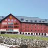 Gro&szlig;es rotes Geb&auml;ude des Jufa Sport Resorts in einer bergigen Landschaft.