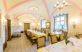 Eleganter Speisesaal mit gedeckten Tischen, Kronleuchtern und Kachelofen.