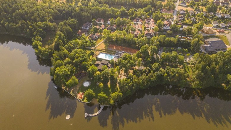 Luftaufnahme eines Ferien- und Theatervillages am See mit Bäumen und Gebäuden.