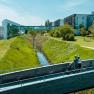 Zwei Radfahrer auf einer Br&uuml;cke vor der Therme Laa & Hotel.