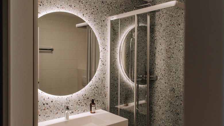 Modernes Badezimmer mit beleuchtetem Spiegel und Dusche.