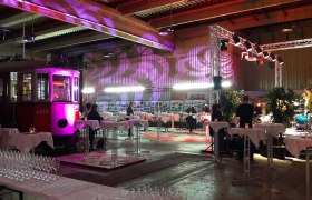 Innenansicht eines Veranstaltungsraums mit einer alten Stra&szlig;enbahn, Tischen und Beleuchtung.