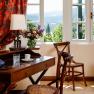 Ein elegantes Zimmer mit Holzm&ouml;beln, einem Schreibtisch, St&uuml;hlen und einem Fenster mit Blick auf eine gr&uuml;ne Landschaft.