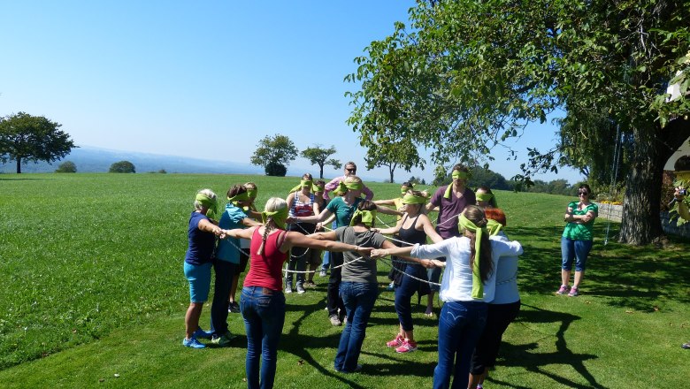 Gruppe von Menschen mit verbundenen Augen bei einer Teamübung im Freien.