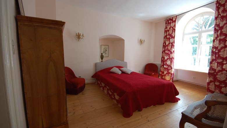 Ein gem&uuml;tliches Schlafzimmer mit rotem Bett, roten Vorh&auml;ngen und Holzm&ouml;beln.