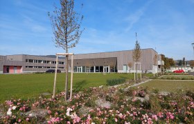 Moderne Geb&auml;ude mit Holzfassade und gepflegter Gartenanlage im Vordergrund.